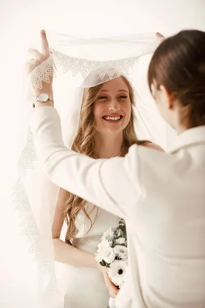 Une mariée sourit joyeusement alors que son partenaire ajuste son voile lors de leur cérémonie de mariage. — Photo de stock