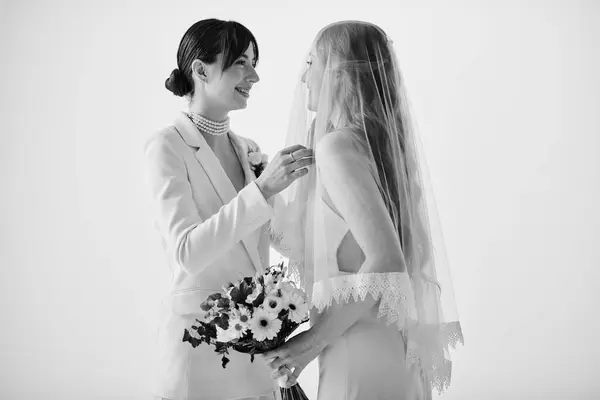 Duas noivas de traje branco compartilham um momento terno enquanto se preparam para seu casamento. A noiva no terno ajusta seu véu parceiros. — Fotografia de Stock