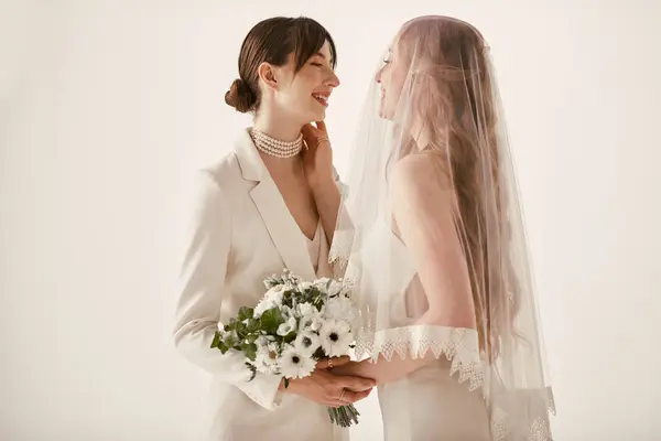 Two brides, one in a white suit and the other in a white dress with a veil, share a loving embrace during their wedding ceremony. — Stock Photo