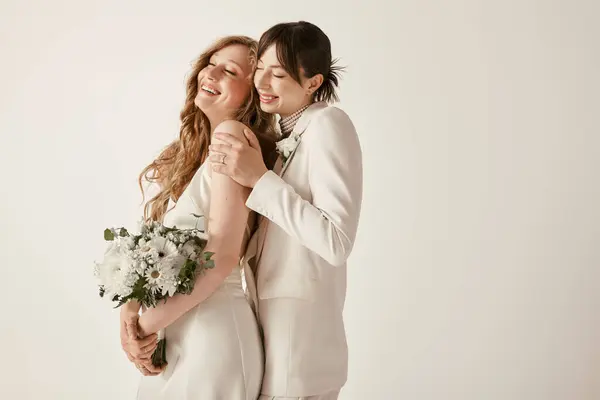 Dos novias en traje blanco abrazan el día de su boda, llenas de alegría y amor. - foto de stock