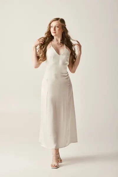 Una bella giovane sposa posa in un abito da sposa bianco fluente su uno sfondo bianco. — Foto stock