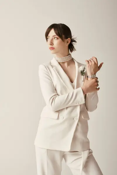 Una hermosa novia joven posa en un traje blanco, una versión contemporánea de la moda nupcial tradicional. Lleva un collar de perlas y una sola flor blanca, añadiendo un toque de encanto clásico. - foto de stock