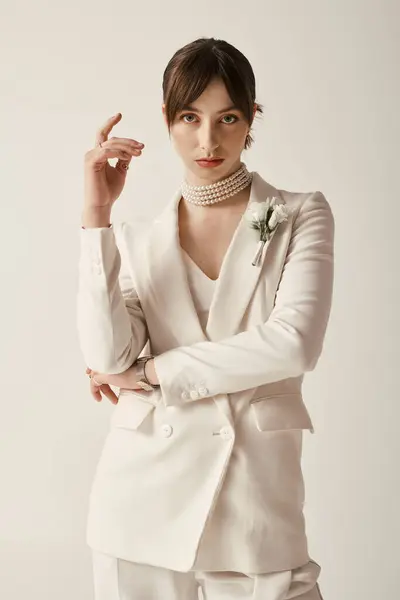 Una hermosa joven con un traje blanco y un collar de perlas se levanta sobre un fondo blanco. - foto de stock
