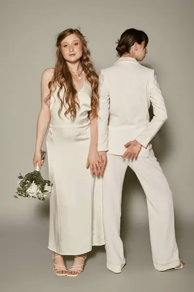 Two young women dressed in white wedding attire pose against a grey backdrop. — Stock Photo
