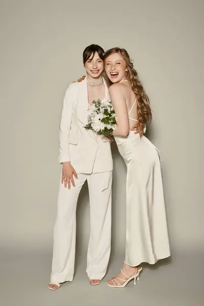 Zwei Frauen in weißen Gewändern posieren lächelnd und mit einem Blumenstrauß für ein Hochzeitsporträt. — Stockfoto