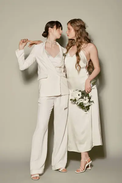 Two women in white attire, one wearing a suit and the other a dress, embrace during their wedding ceremony. — Stock Photo
