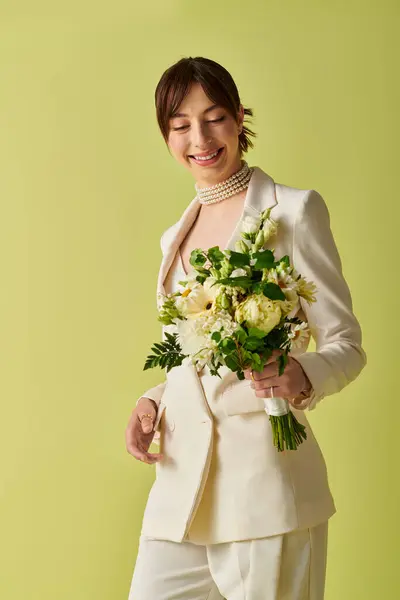 Una sposa, vestita di bianco, sorride dolcemente mentre tiene un mazzo di fiori su uno sfondo verde brillante. — Foto stock