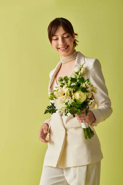 A bride, dressed in white, smiles softly as she holds a bouquet of flowers against a bright green background. — Stock Photo