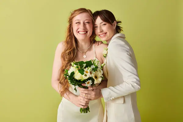 Due donne in abito da sposa bianco sorridono per la fotocamera, una con in mano un mazzo di fiori bianchi. — Foto stock