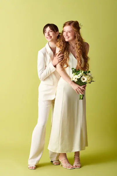 Two young women in white attire celebrate their wedding day with a joyous smile, standing together against a green backdrop. — Stock Photo