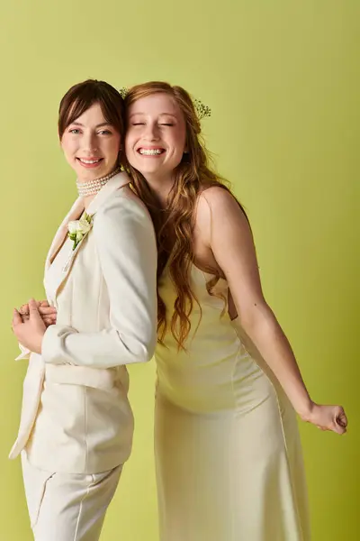 Two brides in white wedding attire smile happily against a green backdrop. — Stock Photo