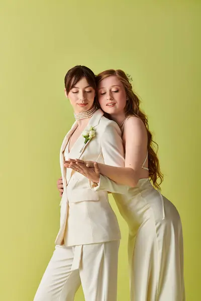 Duas jovens mulheres vestidas de branco abraçam-se durante sua cerimônia de casamento, celebrando seu amor contra um pano de fundo verde.. — Fotografia de Stock
