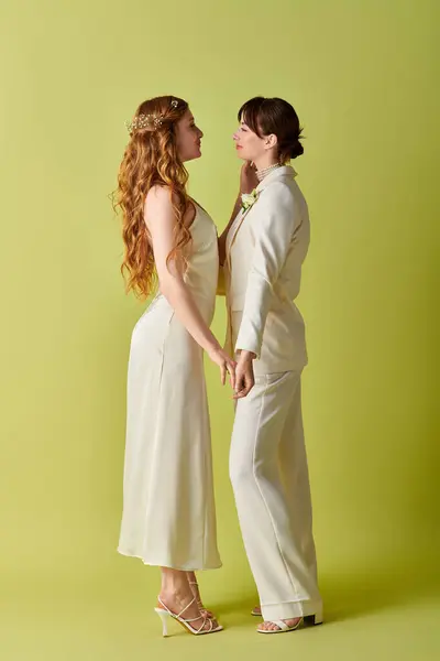 A lesbian couple in white attire stands close together on a green background during their wedding ceremony. — Stock Photo