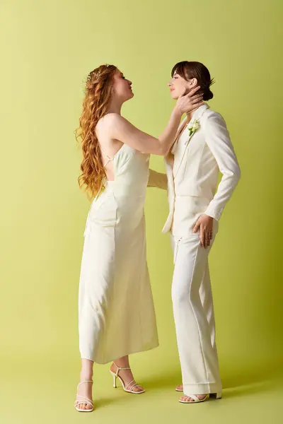 A lesbian couple dressed in white wedding attire stand facing each other against a green backdrop. — Stock Photo