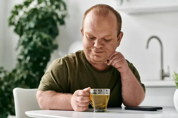 A man with inclusivity sits at a table in his home, enjoying a cup of tea. — Stock Photo