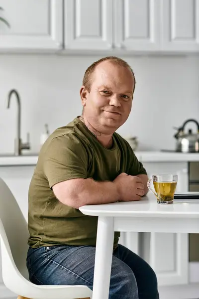 A man with inclusivity sits at a kitchen table, enjoying a cup of tea. — Stock Photo