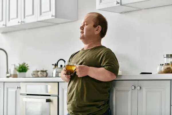 A man with inclusivity stands in his kitchen, casually dressed, enjoying a cup of tea. — Stock Photo
