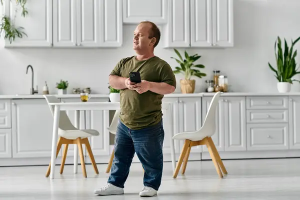 A man with inclusivity stands in his kitchen, holding a phone and smiling. — Stock Photo