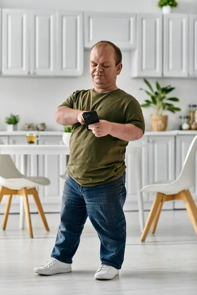 A man with inclusivity in casual attire stands in his home, looking at his phone. — Stock Photo
