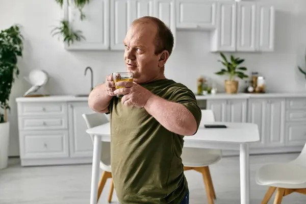 A man with inclusivity in casual clothing stands in his kitchen, holding a glass of liquid, taking a moment to relax. — Stock Photo