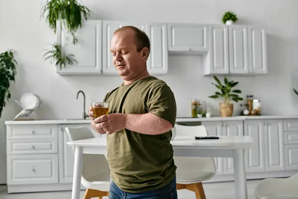 A man with inclusivity stands in his kitchen, casually dressed, holding a cup of tea. — Stock Photo