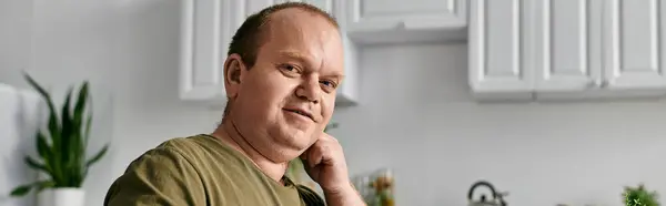 A man with inclusivity sits casually in a kitchen, reflecting on his thoughts. — Stock Photo