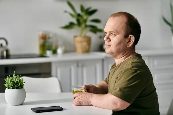 Un uomo con inclusività in abbigliamento casual gode di una bevanda a casa, contemplando il giorno prima. — Foto stock