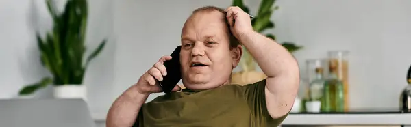 A man with inclusivity in casual attire sits at home talking on the phone. — Stock Photo