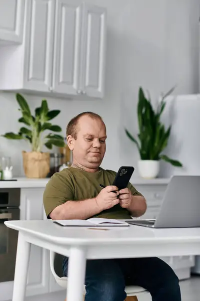 A man with inclusivity sits at a table in his kitchen, casually dressed, looking at his phone. — Stock Photo