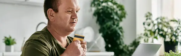 Un homme avec inclusivité en tenue décontractée détient une carte de crédit alors qu'il est assis à la maison. — Photo de stock