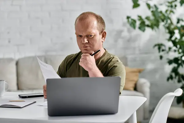 A man with inclusivity sits at his desk in a casual setting, reviewing documents and pondering his next move. — Stock Photo