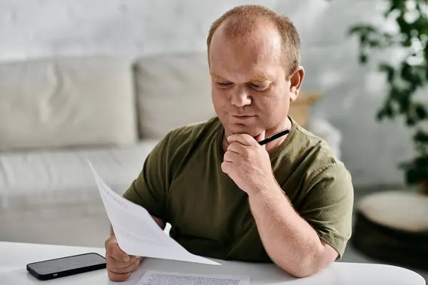 A man with inclusivity sits at a table, thoughtfully reviewing a document. - foto de stock