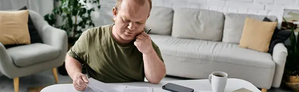 A man with inclusivity sits at a table in his living room, thoughtfully reviewing documents. - foto de stock