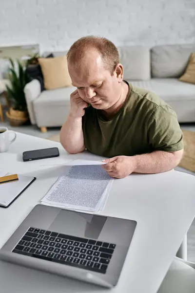 Um homem com inclusividade senta-se em sua mesa, revisando papéis pensativamente. — Fotografia de Stock