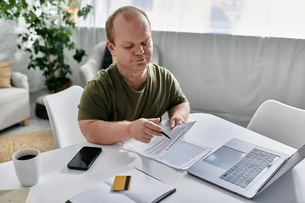Un uomo con inclusività siede a un tavolo nella sua casa, guardando attentamente un documento. — Foto stock