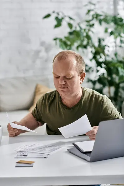 A man with inclusivity in casual attire sits at a table, reviewing documents. — Stockfoto