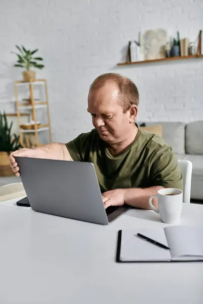 Ein Mann mit Inklusion sitzt an einem Tisch in seinem Homeoffice und arbeitet an seinem Laptop. — Stockfoto