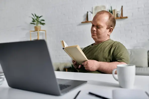Чоловік з інклюзивністю сидить за столом у себе вдома, читаючи книгу. — стокове фото