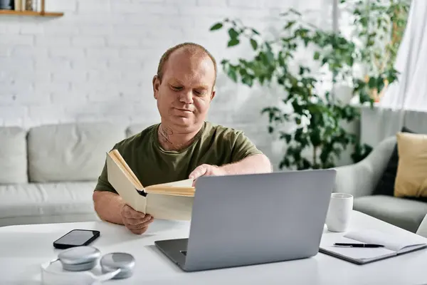 A man with inclusivity sits at a table reading a book, surrounded by the comforts of home. - foto de stock