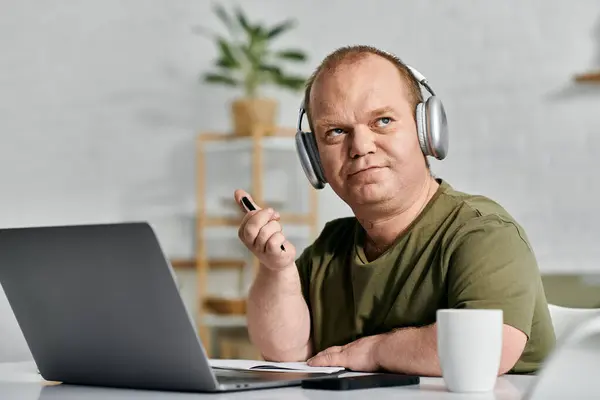 Чоловік з інклюзивністю у навушниках сидить за своїм столом у своєму домашньому офісі, працюючи. — стокове фото