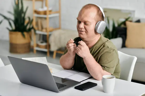 A man with inclusivity wearing headphones sits at a desk in his home office, working on a laptop. — Stock Photo