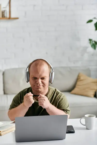 A man with inclusivity wearing headphones sits at a desk with a laptop, looking focused on his work. — Stock Photo