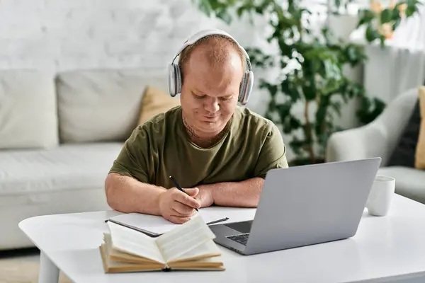 A man with inclusivity wearing headphones studies at home, surrounded by cozy furniture. — Stock Photo