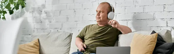 A man with inclusivity sits on a couch at home, wearing headphones and looking relaxed. — Stock Photo