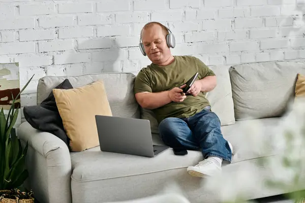 Um homem com inclusividade usando fones de ouvido senta-se casualmente em um sofá, desfrutando de um momento de relaxamento. — Fotografia de Stock