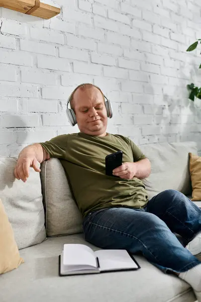 A man with inclusivity wearing headphones relaxes on a couch in his home. — Stock Photo