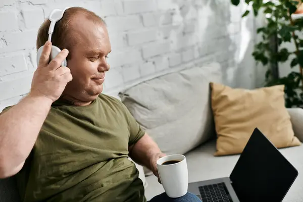 Ein Mann in Freizeitkleidung genießt eine Tasse Kaffee und Musik, während er es sich zu Hause auf der Couch gemütlich macht. — Stockfoto