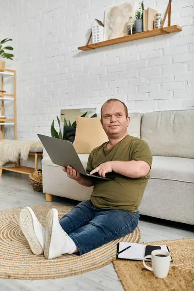 A man with inclusivity sits on the floor, comfortably using a laptop in his home. — Stock Photo