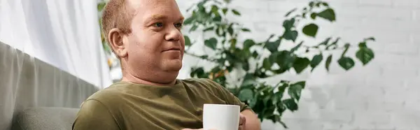 Ein Mann in Freizeitkleidung genießt einen Moment der Ruhe zu Hause, hält eine Tasse Kaffee in der Hand. — Stockfoto