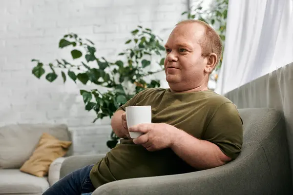 Un homme avec inclusivité en tenue décontractée s'assoit sur un canapé, dégustant une tasse de café dans une atmosphère détendue. — Photo de stock